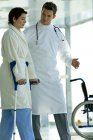 Male doctor assisting female patient in walking on crutches in hospital — Stock Photo