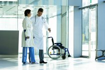 Male doctor assisting female patient in walking on crutches in hospital — Stock Photo