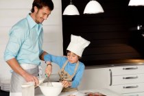 Homem adulto médio fazendo um bolo com seu filho na cozinha — Fotografia de Stock