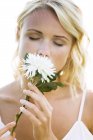 Portrait of young blond woman with eyes closed holding white flower — Stock Photo