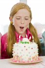 Крупный план рыжей девушки задувающей свечи из праздничного торта — стоковое фото