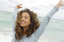 Gros plan d'une adolescente heureuse debout sur la plage avec les bras en l'air — Photo de stock