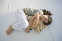Улыбающаяся маленькая девочка спит с плюшевым мишкой на кровати — стоковое фото