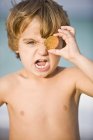 Portrait of screaming little boy covering eye with coin on beach — Stock Photo