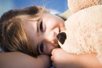 Lächelndes kleines Mädchen kuschelt Teddybär im Sonnenlicht — Stockfoto