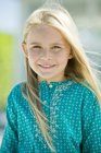 Porträt eines lächelnden kleinen blonden Mädchens, das auf verschwommenem Hintergrund in die Kamera blickt — Stockfoto