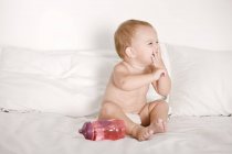 Baby girl laughing on bed with bottle — Stock Photo