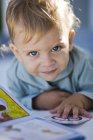 Porträt eines kleinen Jungen, der Bilderbuch liest und in die Kamera blickt — Stockfoto