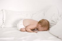 Shirtless baby girl crying on bed — Stock Photo