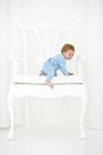 Smiling baby boy getting out of huge white armchair — Stock Photo