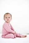 Baby girl in pink pajamas sitting on bed on white background — Stock Photo