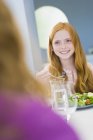 Усміхнена руда дівчина їсть салат за столом — стокове фото
