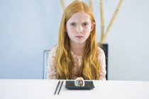Portrait of angry ginger girl sitting at dining table with sushi — Stock Photo