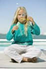 Girl blowing soap bubbles with bubble wand on beach — Stock Photo