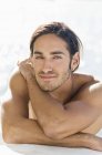 Portrait of sensual shirtless young man leaning on elbows at sea water — Stock Photo