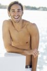 Ritratto di giovane uomo sorridente senza maglietta in piedi sulla riva del lago — Foto stock