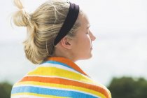 Visão traseira da mulher com toalha de praia em torno dos ombros relaxante na natureza — Fotografia de Stock