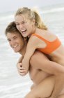 Alegre homem dando mulher piggyback passeio na praia — Fotografia de Stock