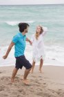 Cheerful couple walking holding hands on beach — Stock Photo