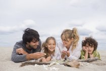 Happy family relaxing on beach, lying in sand with seashells — Stock Photo