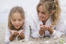 Woman lying with daughter lying on beach with seashells — Stock Photo