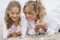 Frau liegt mit Tochter am Strand mit Muscheln — Stockfoto