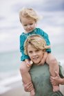Niño llevando hermana en hombros en la playa - foto de stock