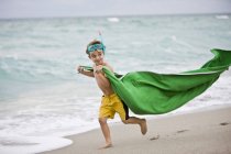 Niño con máscara de buceo corriendo en la playa con pareo verde - foto de stock