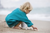 Kleines Mädchen spielt mit Muscheln am Strand — Stockfoto