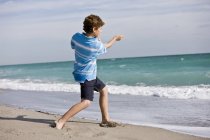 Хлопчик кидає камінь у море на пляжі — стокове фото