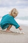 Маленькая девочка играет с раковинами на пляже — стоковое фото
