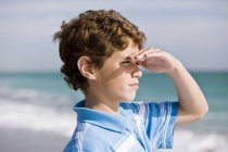 Nahaufnahme eines Jungen, der am Strand steht und aufs Meer blickt — Stockfoto