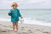 Petite fille tenant seau de sable sur la plage — Photo de stock
