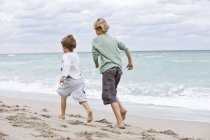 Вид на веселых мальчишек, бегущих по песчаному пляжу — стоковое фото