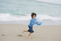 Веселый мальчик играет с мячом на пляже — стоковое фото