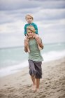 Мальчик носит сестру на плечах на пляже — стоковое фото