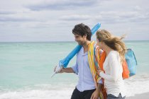Couple walking on beach with bag and umbrella under cloudy sky — Stock Photo