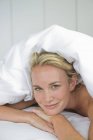 Close-up of woman lying on bed under duvet and smiling — Stock Photo