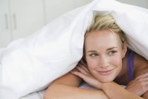 Primer plano de la mujer acostada en la cama bajo edredón y sonriendo - foto de stock
