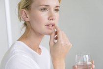 Woman taking Omega-3 capsule and holding glass of water — Stock Photo