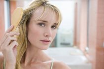 Junge blonde Frau beim Haareputzen im Badezimmer — Stockfoto