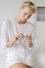 Woman holding blister pack of medicine while sitting on bed — Stock Photo