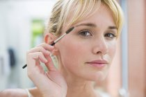 Close-up of blond young woman using eyebrow brush — Stock Photo