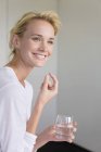 Sorrindo jovem mulher tomando cápsula Omega-3 e segurando vidro de água — Fotografia de Stock