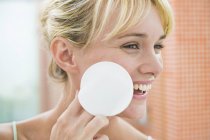 Жінка сміється, застосовуючи порошок для обличчя з бавовняною кулькою — стокове фото