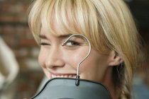 Close-up of blond smiling woman with hanger winking in boutique — Stock Photo