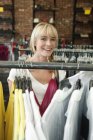 Happy blond woman choosing dresses in boutique — Stock Photo