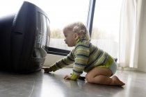 Piccolo bambino accendere la TV mentre seduto sul pavimento a casa — Foto stock