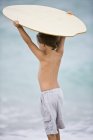Rear view of little boy holding a body board over head on beach — Stock Photo