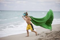 Мальчик в маске с аквалангом бегает по пляжу с зеленым парео — стоковое фото